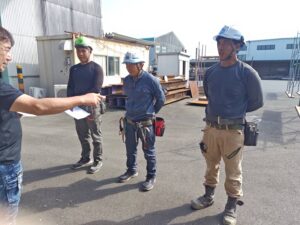 足場の技能試験会場で、ヘルメットを着用して説明を聞くエリクソンさんと受験者たち