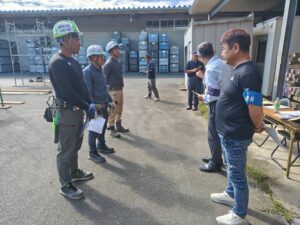 足場の技能試験会場で、ヘルメットを着用した受験者たちが関係者から説明を受けている様子