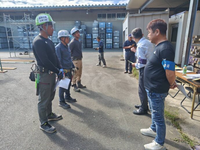 足場の技能試験会場で、ヘルメットを着用した受験者たちが関係者から説明を受けている様子