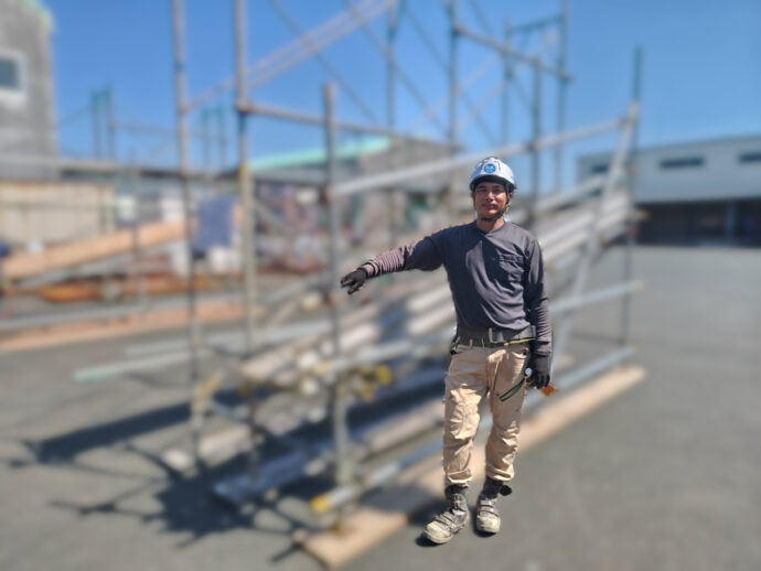 足場の前でヘルメットと作業着を着用して立つ実習生のエリクソンさん