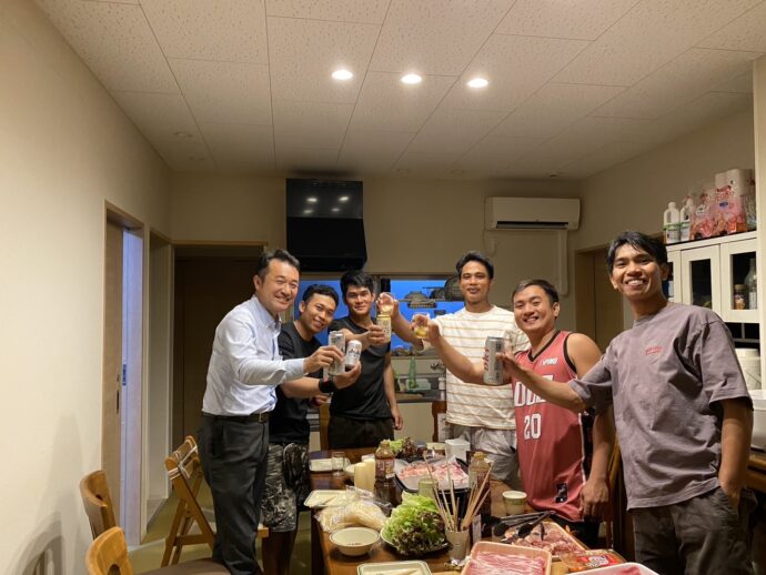 アルバートさんのおかえりなさいの焼肉パーティー|豊川市宿町 実習生たちと社長が食卓を囲み、飲み物を手に乾杯している様子